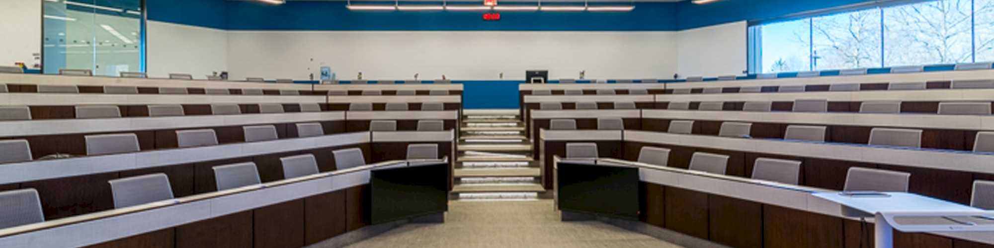 An empty, modern lecture hall with rows of tiered seating, a podium in the front, and a bright, well-lit atmosphere.