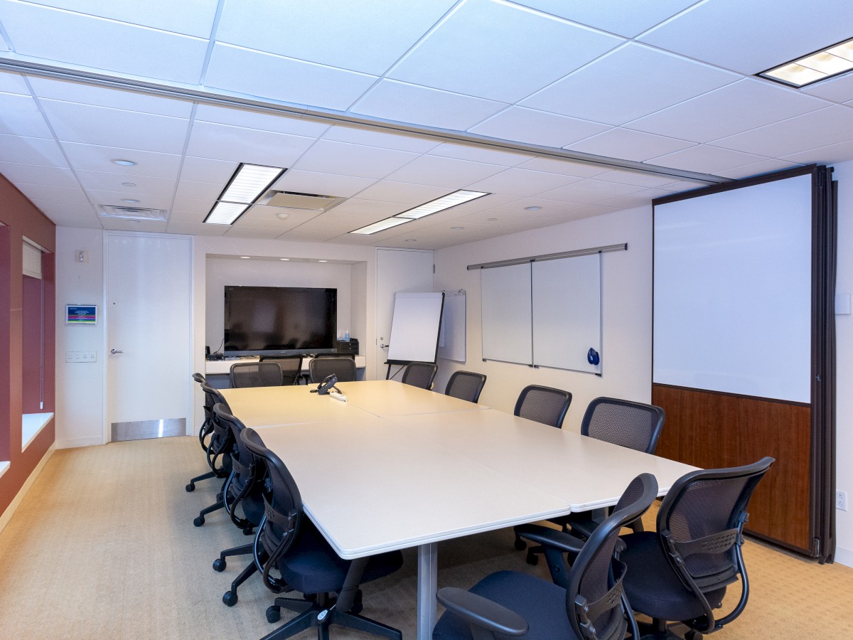 A modern conference room with a long table, several office chairs, a large wall-mounted TV, a whiteboard, and a flip chart stand ends the sentence.