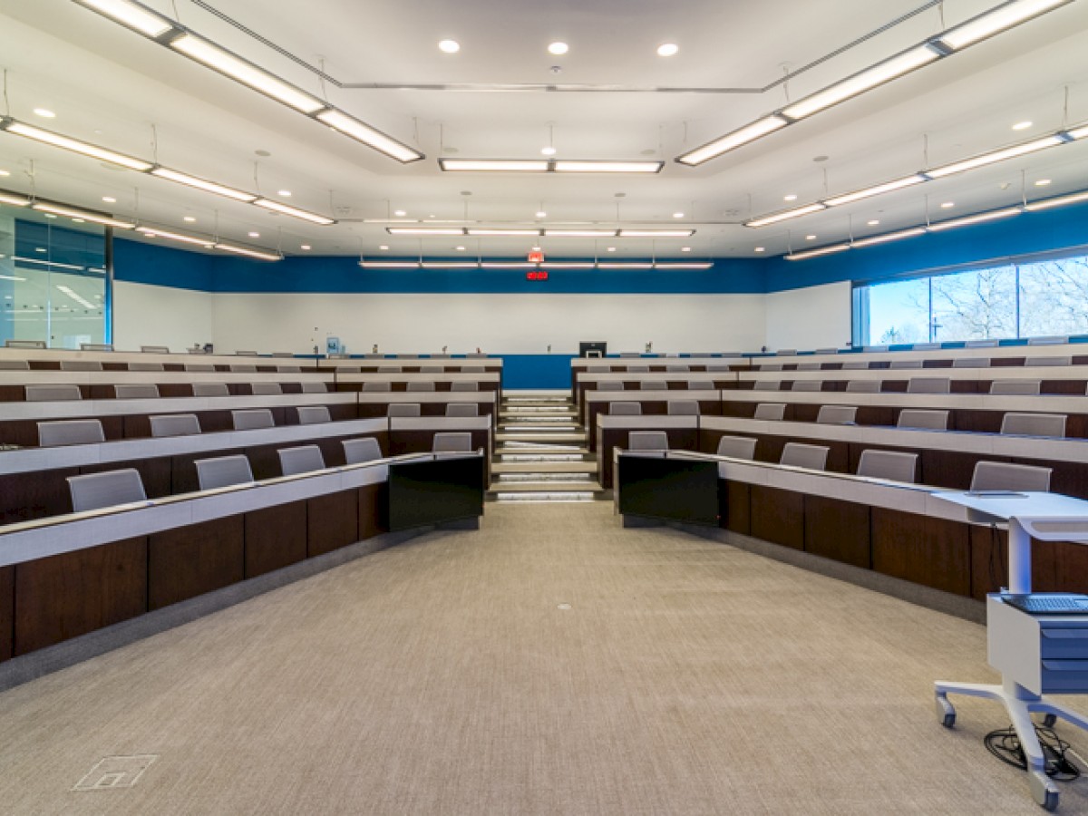 The image shows a modern lecture hall with tiered seating, a podium, and wide windows, designed for academic presentations or conferences.