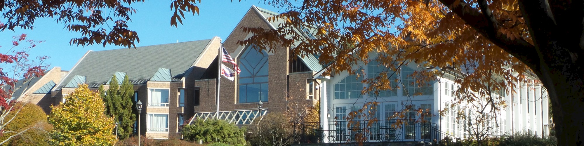 A large building complex with modern architectural elements is surrounded by lush green lawn and autumn trees under a clear blue sky.