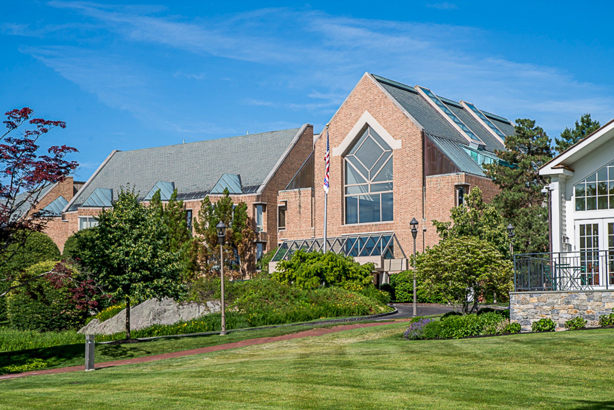 A large brick building with a modern design, surrounded by lush greenery and a well-manicured lawn under a clear blue sky.