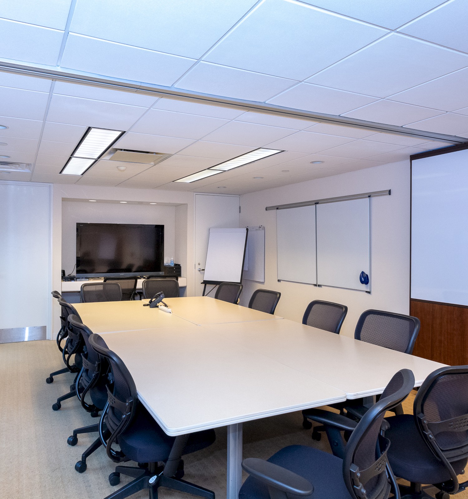 This image shows a modern conference room with a long table, chairs, a whiteboard, and a wall-mounted TV, suitable for business meetings.